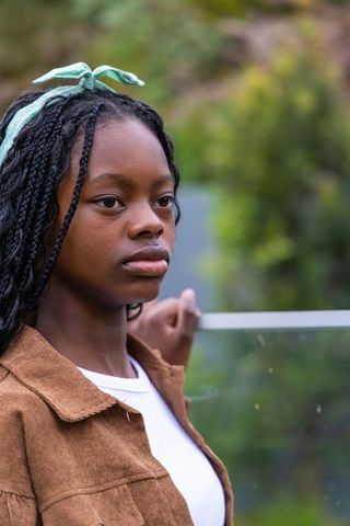 Teen african american leaning on glass balcony wearing mint headscarf and corduroy jacket