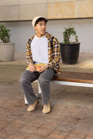 Asian student sitting on bench holding apple and notebook wearing beanie and plaid shirt