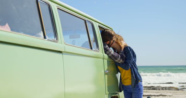 Woman resting her head on a green vintage camper van by a beach, showcasing a relaxed and peaceful vacation vibe. This can be used for travel blogs, holiday advertisements, or lifestyle articles emphasizing outdoor adventures and relaxation at the seaside.
