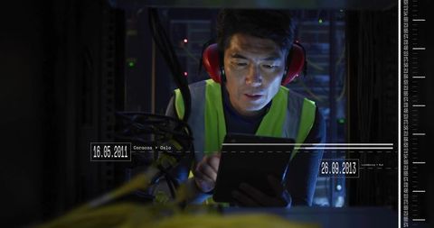 Network Technician Inspecting Server Rack with Tablet Wearing Hi-Vis Vest and Earmuffs