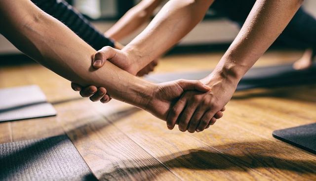 Partner yoga clasping forearms supporting balance and strength on wooden studio floor