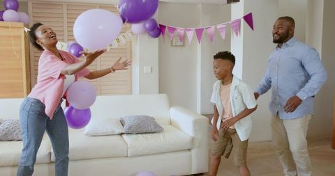 African American Family Celebrating at Home Tossing Purple Balloons in Living Room