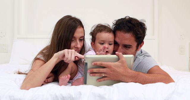 Loving parents with baby daughter using tablet on the bed