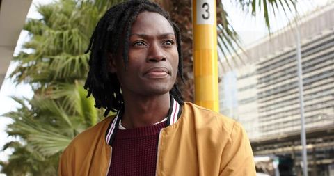 African american man standing at urban transit stop in mustard jacket and maroon sweater