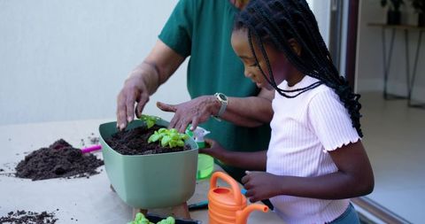 Senior african woman teaching young african girl planting herbs in planter on patio