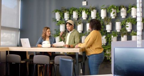 Diverse team discussing project plans at high table with living green wall and laptop