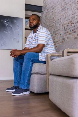 African man sitting on light-gray sofa in modern minimalist lounge relaxed home lifestyle