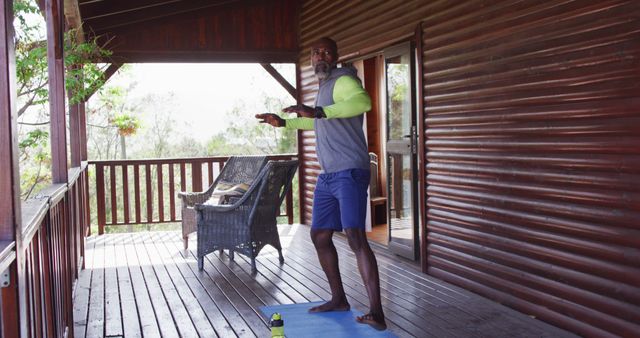 Happy senior african american man spending time in log cabin, doing yoga and stretching. Free time, domestic life and nature concept.