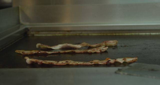 Close up of slice bacon rashers frying on a plate sheet in a busy restaurant kitchen. Busy chefs at work in commercial kitchen.
