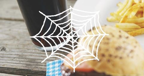 Rustic sesame burger resting on wooden table with fries and cola, spiderweb overlay