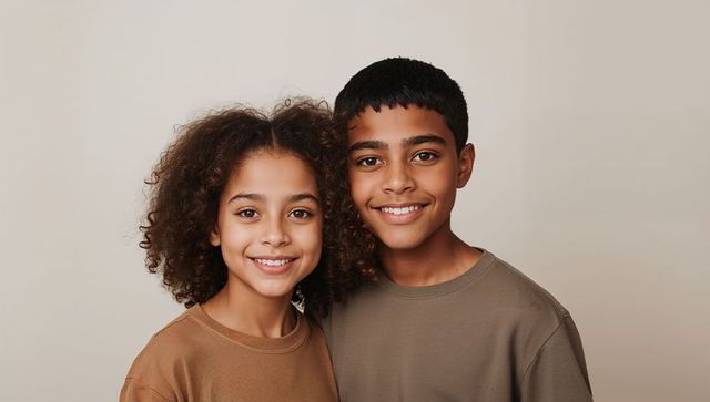 Smiling preteen brother and sister wearing neutral crew-neck shirts studio portrait