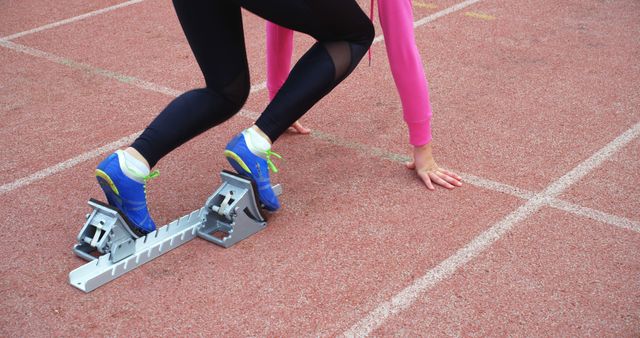 Close-up of a diverse pair of athletes at the starting blocks on a track field, ready to sprint, with copy space. Their poised stance and specialized footwear highlight the competitive nature of track and field events.