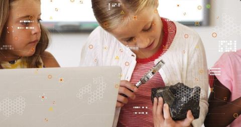 Students examining rock with magnifier in stem classroom using laptop for science learning