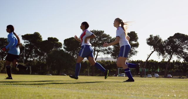 Female soccer players actively running on a field during a match on a sunny day. Ideal for illustrating team sports, women's athletics, outdoor physical activities, fitness and health-related themes. Suitable for use in sports campaigns, women's empowerment projects, and healthy lifestyle promotions.