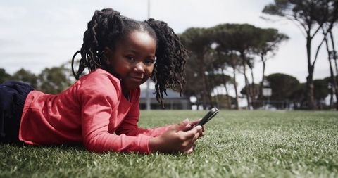 Young Girl Relaxing on Grass with Smartphone Outdoors