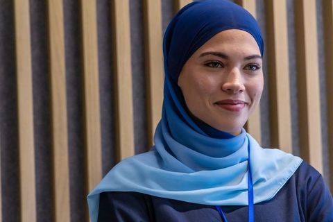 Young professional woman wearing two-tone blue headscarf smiling at conference portrait