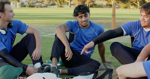 Multiethnic cricket teammates sitting on field relaxing and chatting after practice