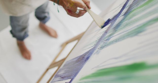 Artist engaged in the creative process of painting abstract art on canvas, using a brush to apply colors in a studio. Ideal for use in blogs, websites, or marketing materials related to art, creativity, artistic expression, and studios.