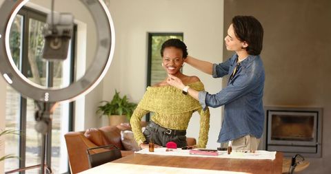 Stylist adjusting hair and makeup on smiling african american model in home studio
