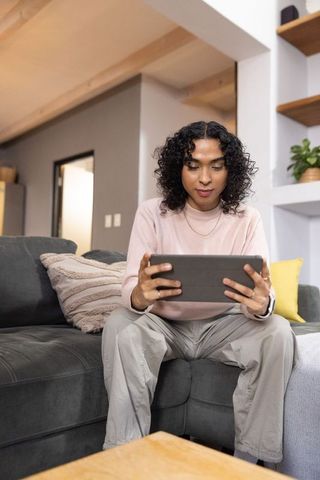 Nonbinary person using tablet on gray sofa in modern living room