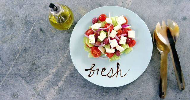 A plate of Greek salad sits on a table, with the word fresh stylishly written beside it, evoking a sense of healthy eating. Olive oil and utensils complement the meal, emphasizing the Mediterranean diet's focus on fresh ingredients and simplicity.