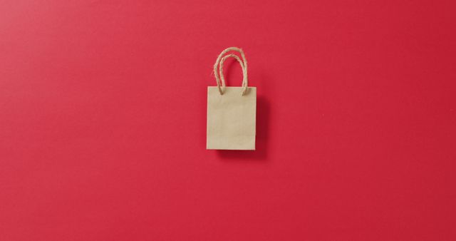 Small brown gift bag with string handles on red background with copy space. Shopping, sale and retail concept digitally generated image.