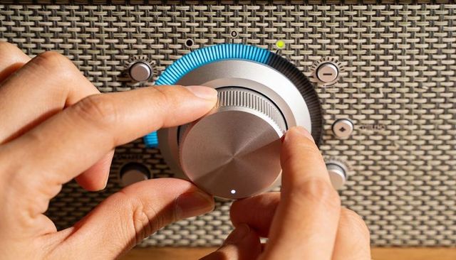 Turning hands adjusting vintage metal dial on woven speaker grille with blue indicator