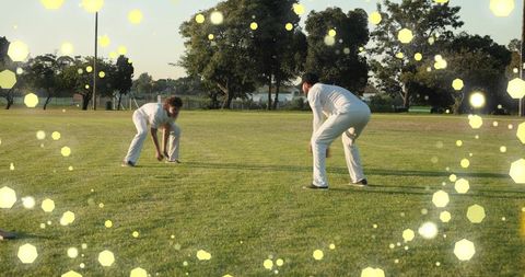 Two Cricket Fielders Crouching on Sunlit Grass, Teamwork and Focus with Golden Bokeh