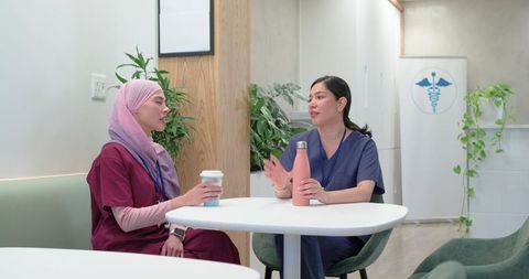 Diverse female healthcare team sharing coffee break in clinic lounge, nurses collaborating