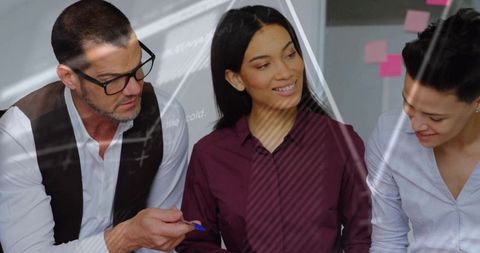 Diverse business team collaborating at glass whiteboard, leader pointing with blue pen