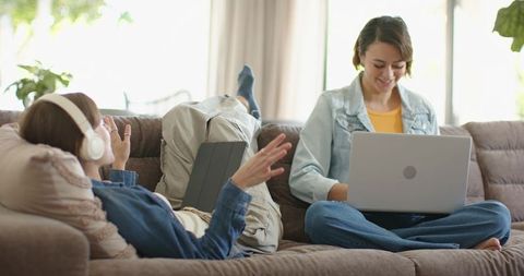 Young women relaxing on couch using laptop and tablet in bright cozy living room