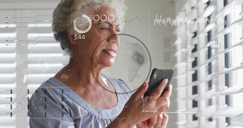Senior woman using smartphone viewing augmented reality hud by window blinds in daylight