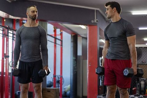 Two men training with hex dumbbells in industrial gym rig for strength workouts