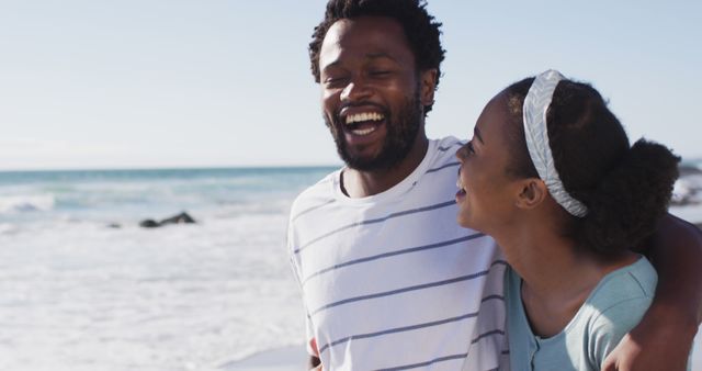 African american couple smiling, embracing and walking on the beach. healthy outdoor leisure time by the sea.