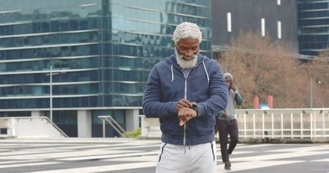Senior African American Man Checking Smartwatch While Walking City Plaza with Hoodie and Glass Facad