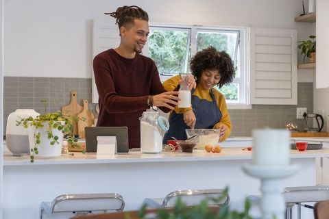 Couple baking together in bright modern kitchen mixing batter and pouring milk