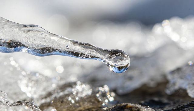 Melting icicle droplet catching sunlight with crystal refraction and sparkling bokeh