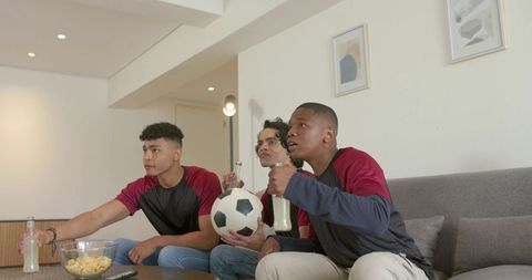 Group watching soccer match on sofa sharing snacks and drinks during live game night