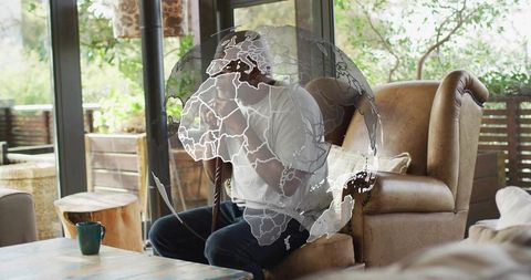 Senior man talking on smartphone while holding cane in cozy living room with globe overlay
