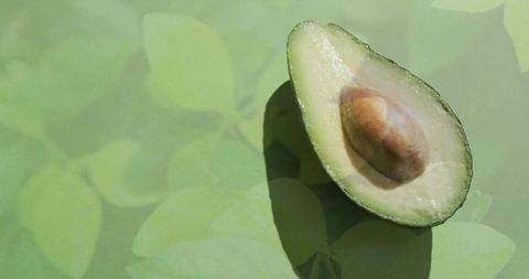 Halved creamy avocado showing seed on soft leaf-pattern backdrop, minimalist green flatlay