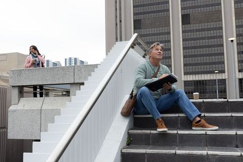 Urban creative duo sitting on concrete steps sketching notebook while checking phone