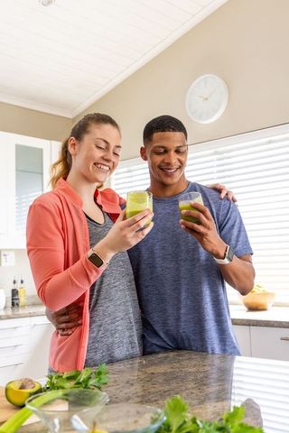 Multiethnic couple enjoying green smoothies in bright kitchen healthy morning routine
