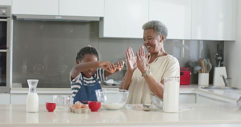 African american grandma guiding granddaughter through baking in bright modern kitchen
