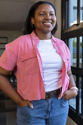 Smiling african american woman at window wearing pink shirt and jeans in sunlit workplace