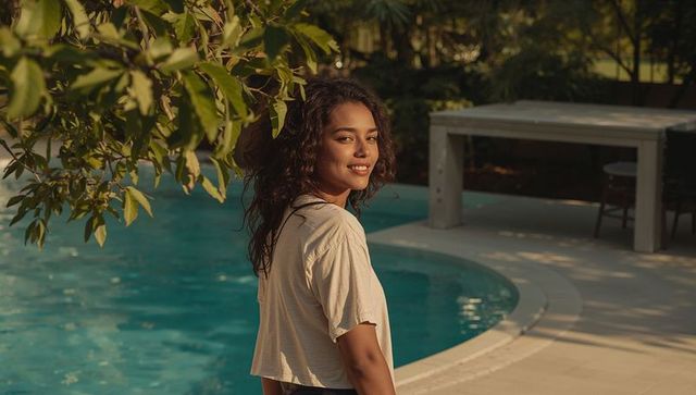 Smiling woman standing by backyard pool during golden hour, relaxed summer lifestyle
