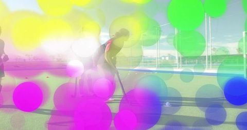 Teen practicing field hockey on seaside turf with pink backpack and colorful bokeh