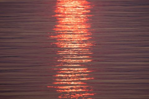 Sunset reflecting and glowing in vertical band on calm water with pink orange ripples