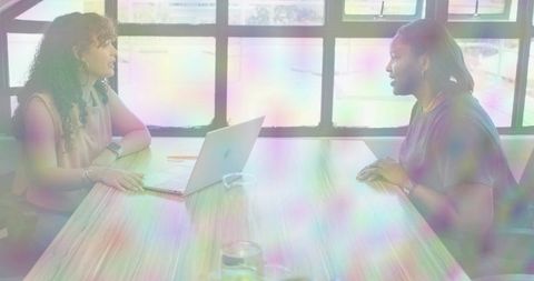 Two women discussing during interview with laptop and carafe in minimalist boardroom