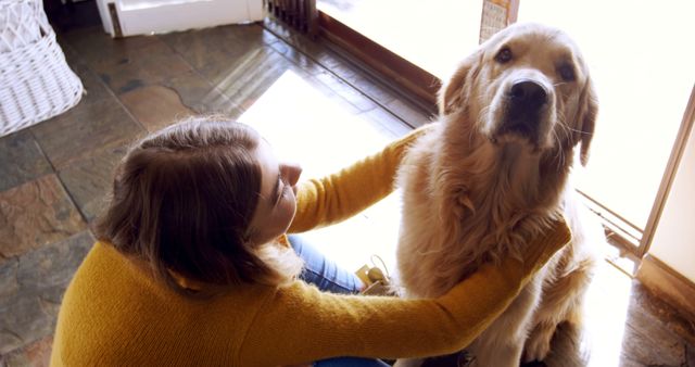 A woman is hugging her golden retriever dog in a sunlit room, creating a warm and cozy atmosphere. This image is perfect for use in pet care advertisements, bonding and companionship themes, and home-related content. It illustrates the affection and special bond between a pet and its owner.