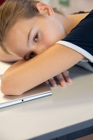 Adolescent girl relaxing on school desk with laptop